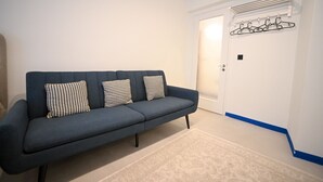 A room with a dark blue sofa, patterned cushions, a white door, and a coat rack with hangers.
