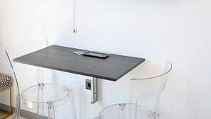 Un salon moderne avec un téléviseur à écran plat fixé au mur, une petite table avec une télécommande et deux chaises transparentes.