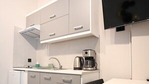 A compact kitchenette with a built-in fridge, a coffee maker, and a flat-screen TV mounted on the wall. - Aura Suite by Zeus suites (Athina)