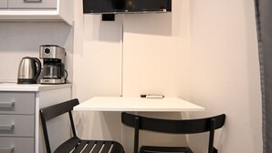 A small kitchenette with a coffee maker, a flat-screen TV mounted on the wall, and two chairs around a small table. - Aura Suite by Zeus suites (Athina)