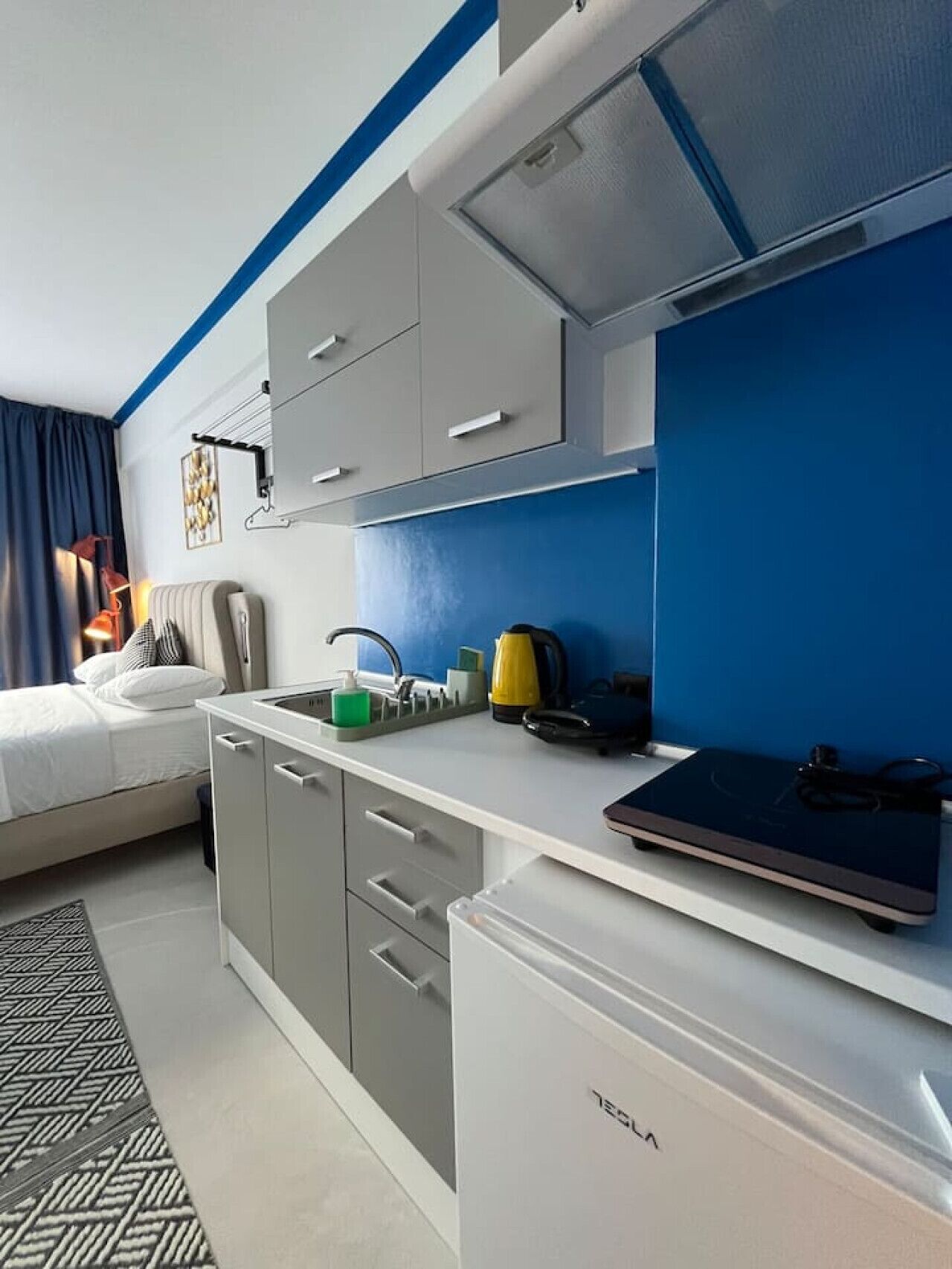 A compact hotel room with a kitchenette, a bed, and a desk area.
