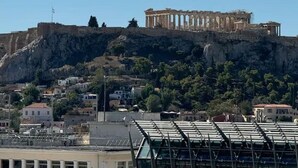 Vue de l’Acropole d’Athènes, avec, au premier plan, des bâtiments modernes et, au loin, les ruines antiques qui se dressent sur une colline.