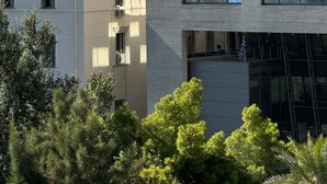 Un bâtiment moderne à la façade de verre, une structure classique en arrière-plan et une végétation luxuriante tout autour.