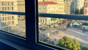 Une vue depuis une fenêtre dont le cadre est en métal, donnant sur un paysage urbain avec différents bâtiments, dont une banque.