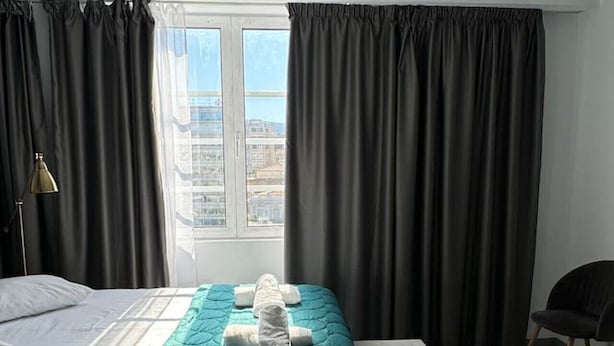Une chambre d’hôtel avec un lit, une banquette, une lampe et une vue sur la ville par la fenêtre.
