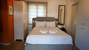 Una cama bien hecha con almohadas y toallas, una lámpara de noche y un armario con espejo.