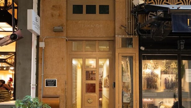 Un edificio con puerta de madera y entrada de vidrio, un letrero que indica restaurante, y una planta en maceta afuera.