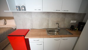 Una kitchenette compacta con un lavamanos, un refrigerador rojo y armarios blancos.