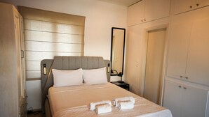 A neatly made bed with white linens and two rolled towels, a bedside table with a lamp, a large mirror, and a wardrobe with multiple doors.