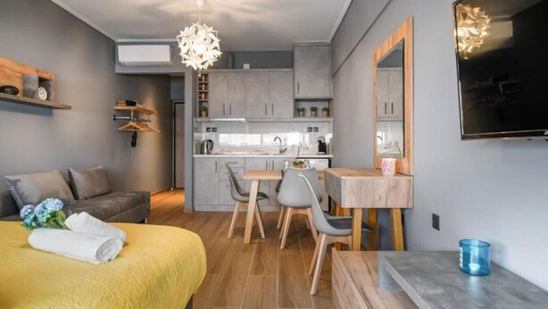 A modern, compact living space with a bed, a dining area, a kitchen, and a TV mounted on the wall.