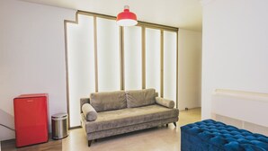 Una sala de estar moderna con un sofá color beige, un refrigerador rojo, un otoman azul y una lámpara colgante roja.