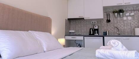 A hotel room with a bed, a small kitchenette, and a bathroom.