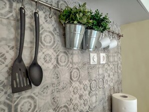 A bathroom with patterned tiles, a toilet paper holder, a spout, and two metal buckets with plants.