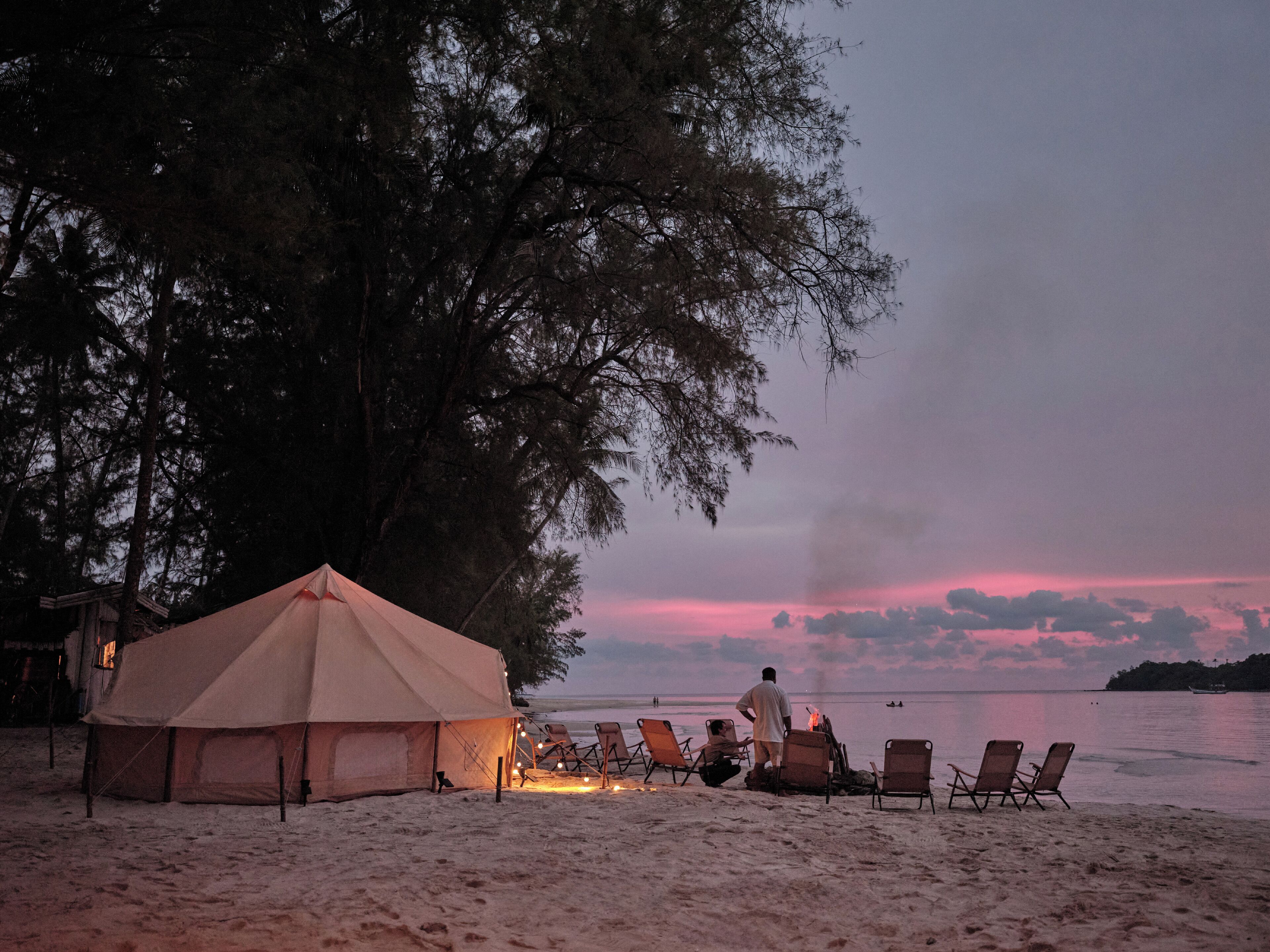 A beach scene with a tent, lounge chairs, and a fire.