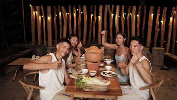 A group of people seated at a wooden table outdoors with a rustic backdrop.