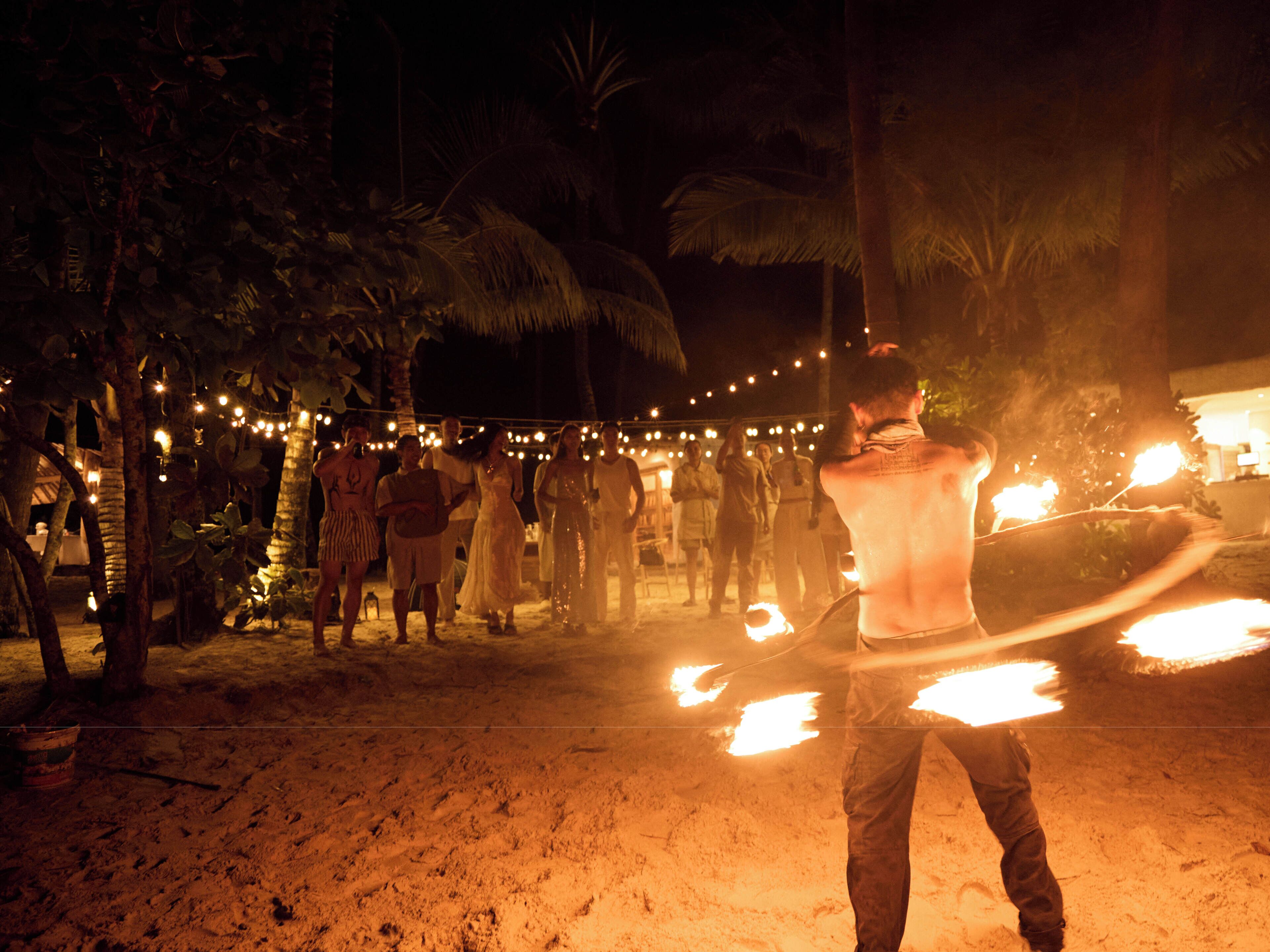 A sandy outdoor area with palm trees and string lights.