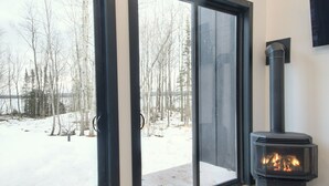 A modern interior with a wood-burning stove, large sliding glass doors leading to a snowy outdoor area, and a high ceiling with skylights.