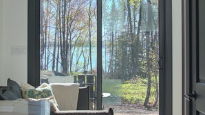 A room with a large sliding glass door leading to a view of trees and a body of water.