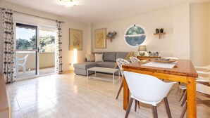 Un salon moderne comprenant un canapé, une table à manger avec des chaises, une table basse et une vue sur un balcon extérieur, accessible par une porte vitrée.