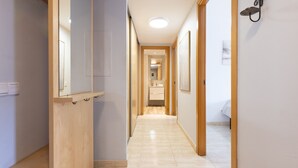 Un couloir étroit, avec des portes en bois et un sol carrelé, qui mène à une salle de bain équipée d’un lavabo et d’un miroir.