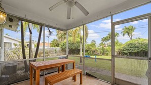 A covered patio with a table and bench, large windows, and a ceiling fan.