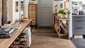 A hallway with a wooden wine rack, a wooden table with books, a dresser, and a kitchen area with a blender and a coffee maker. - Playful Atelier, by Veeve (Paris)