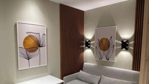 A modern living room with a grey sofa, a white side table, and two wall-mounted light fixtures. - Tirent Apartment-Studio Central (Tirana)
