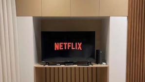A modern entertainment unit with a flat-screen TV displaying the Netflix logo, a soundbar, and a gaming console. - Tirent Apartment-Studio Central (Tirana)