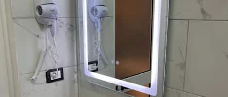 A bathroom with a white sink, a mirror with a lighted frame, and two hair dryers mounted on the wall.