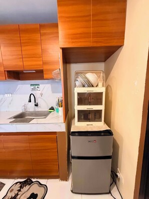 A compact kitchen with wooden cabinets, a sink, and a refrigerator. - Bay Mau Homestay l Cozy 2BR  Exclusive House with generator • Near Dahican beach (Mati)