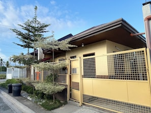 A residential building with a yellow exterior, a gated entrance, and a tree in the foreground.