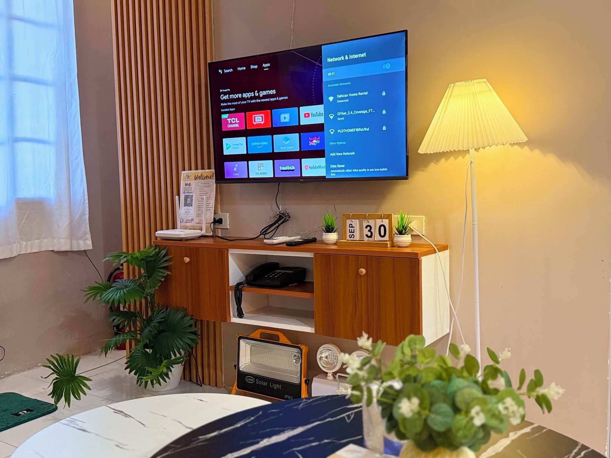 A modern living room with a flat-screen TV mounted on the wall displaying a home screen.
