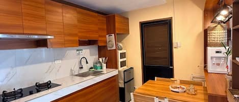 Cocina compacta con armarios de madera, estufa integrada y comedor con mesa y sillas.