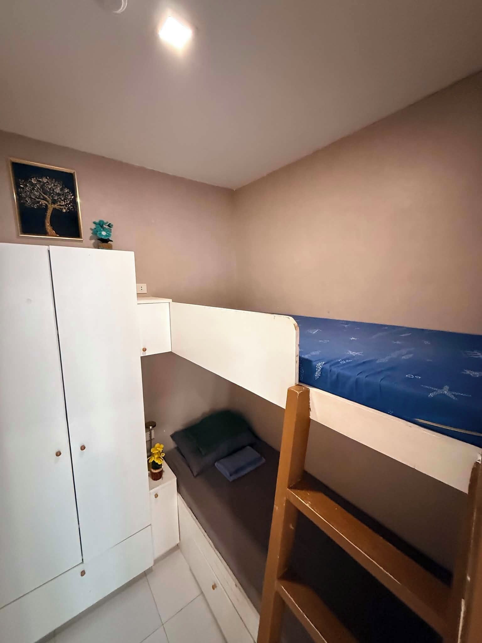 Una habitación pequeña con una cama superpuesta, un armario blanco y una mesita con un jarrón.