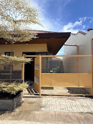 A building with a gated entrance, a small tree, and a paved area.