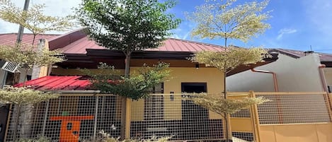 A two-story building with a red roof, a fenced garden area, and a clear sky.