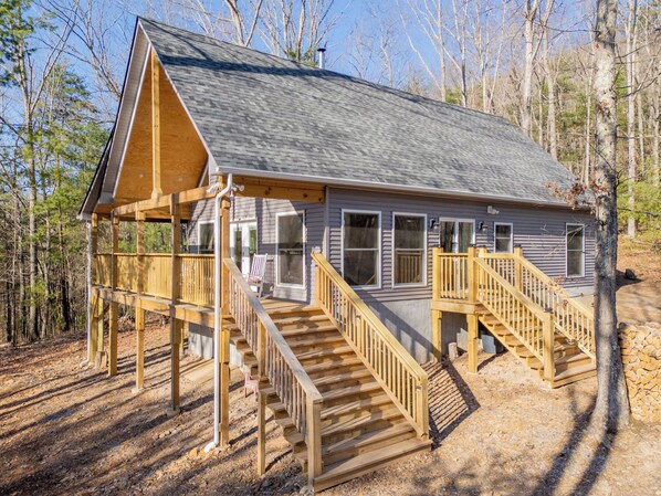 A cabin with a wooden deck, a staircase, and a large window. - Peaceful A-frame cabin with hot tub, forest views, modern comfort, and total privacy in nature. (Radford)
