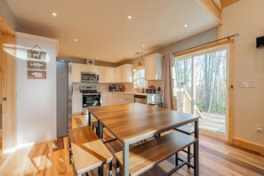 A modern kitchen with white cabinets, stainless steel appliances, and a wooden dining table with benches. - Peaceful A-frame cabin with hot tub, forest views, modern comfort, and total privacy in nature. (Radford)
