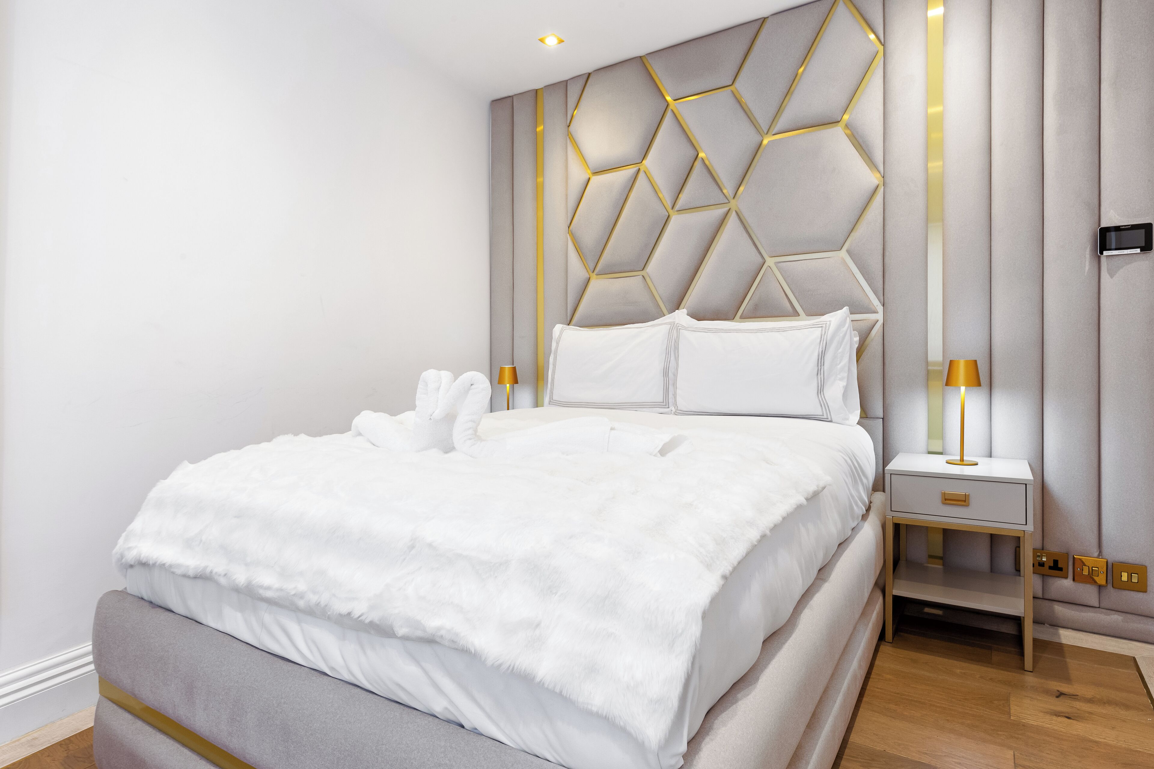 Una habitació d'hotel moderna amb un llit gran, un capçaleria geomètrica, làmpades laterals i una taula de nit.