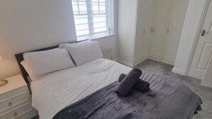 A bedroom with a bed, a nightstand, a window with blinds, a wardrobe, and a hanging light fixture. - 3 Bed House - Sleeps 6 - Parking - Wifi (Maidstone)