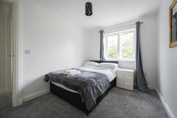 A bedroom with a bed, a nightstand, a window with curtains, and a ceiling light fixture. - 3 Bed House - Sleeps 6 - Parking - Wifi (Maidstone)