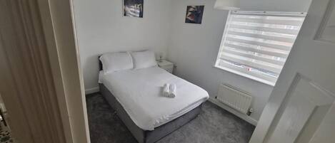 A bedroom with a bed, a nightstand, a window with blinds, and a radiator.