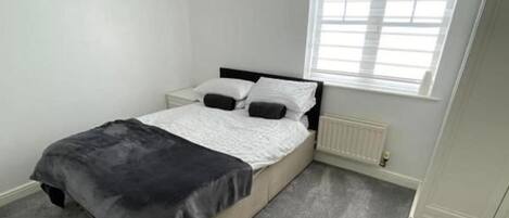 A bedroom with a bed, a radiator, a window, and two wall-mounted pictures.