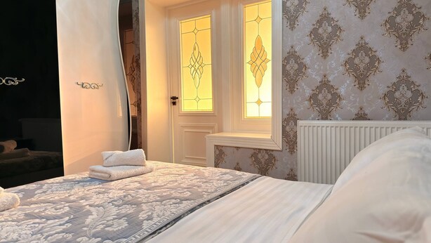 A hotel room with a bed, a nightstand, a mirror, and a window with decorative glass.