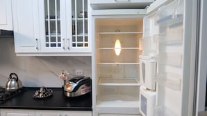 An open refrigerator with a light on, a kettle, and a rice cooker on the counter.