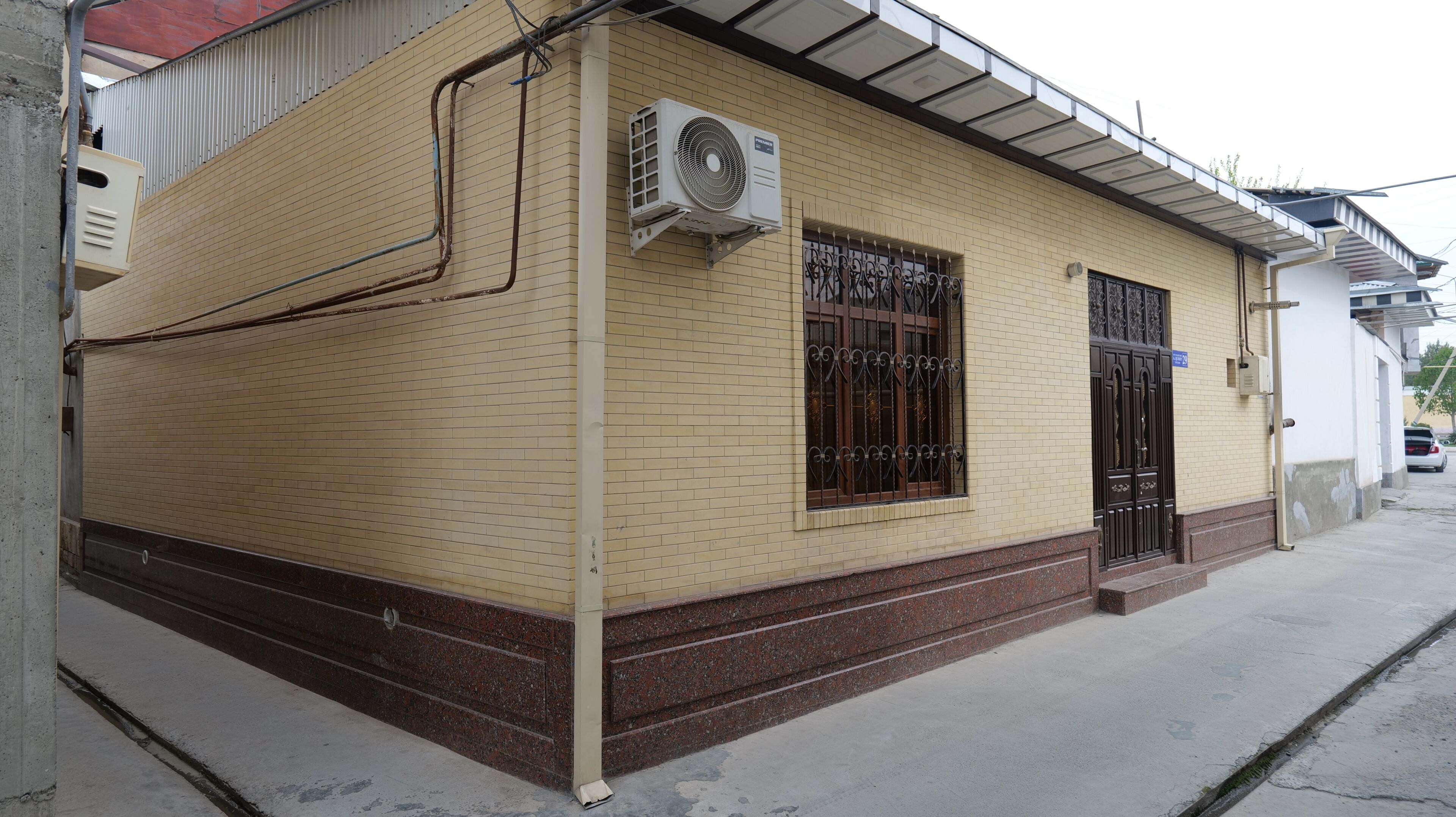 A building with a brick facade, a window with decorative iron bars, and an air conditioning unit mounted on the wall.