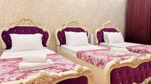 Habitación de hotel con tres camas, cada una con cabecero morado y ropa de cama blanca.