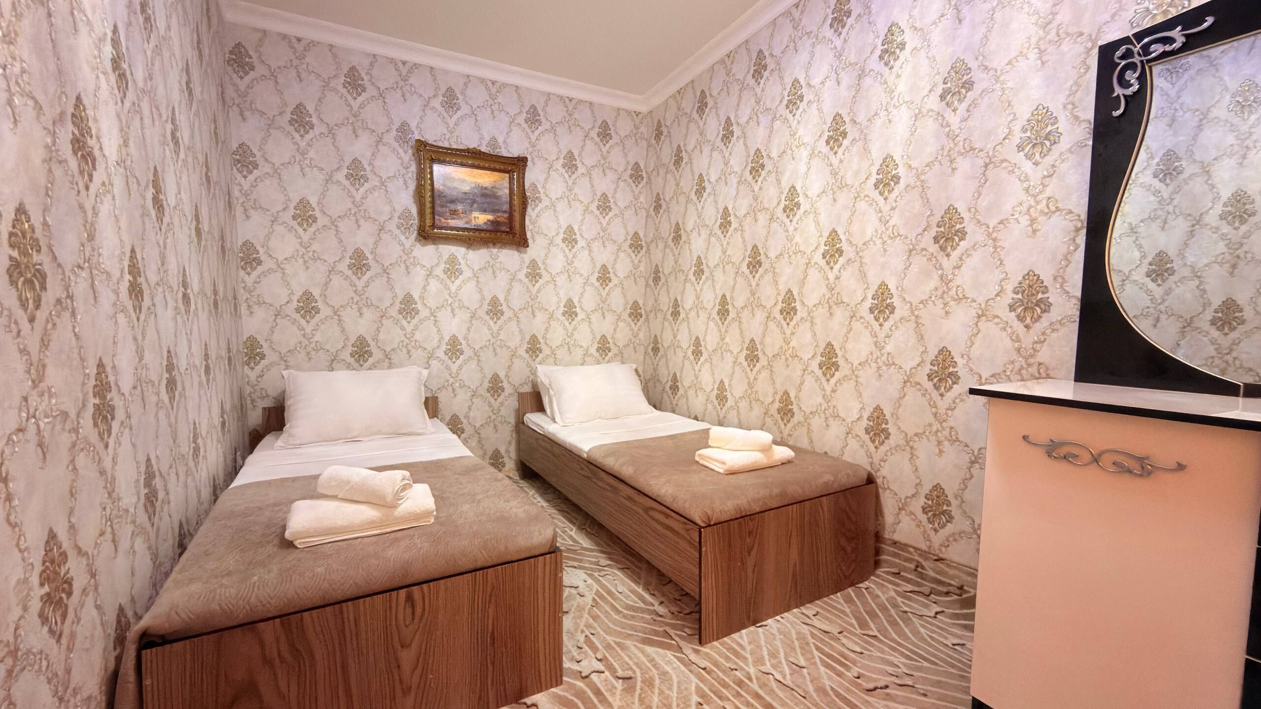 Quarto com duas camas, cômoda de madeira, espelho e um quadro na parede.