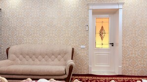 A room with a patterned wallpaper, a beige sofa, a door with a stained glass window, and a red carpet.