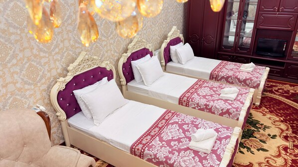 Habitación con dos camas, cada una con cabecero morado y ropa de cama blanca, una silla de madera y una alfombra estampada.